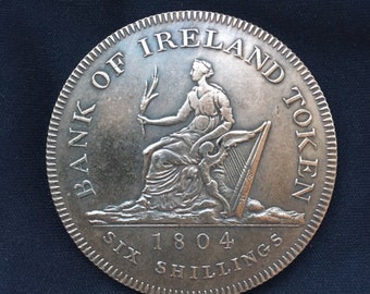 May include: A silver coin with the inscription "Bank of Ireland Token Six Shillings 1804" and a depiction of a woman sitting on a throne with a harp.