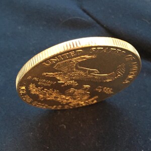 May include: A gold-colored United States of America coin with an eagle design and the words "E Pluribus Unum" and "In God We Trust".