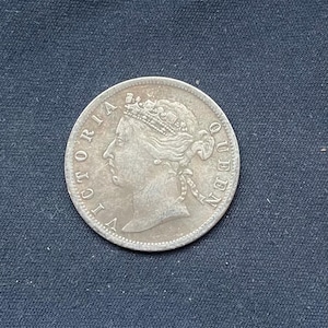 May include: A silver coin featuring a profile of Queen Victoria wearing a crown, with the inscription "VICTORIA QUEEN" around the edge. The coin is circular and has a detailed design, with a slightly worn appearance.