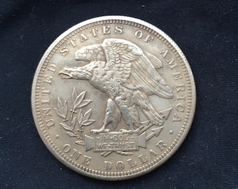 May include: Silver dollar coin with an eagle perched on an arrow and olive branches. The coin reads "United States of America" and "One Dollar" around the edge. The words "In God We Trust" are inscribed on a ribbon held in the eagle's talons.