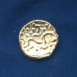 Puede incluir: Una moneda de color dorado con un diseño de león. La moneda tiene un borde elevado y una superficie lisa.
