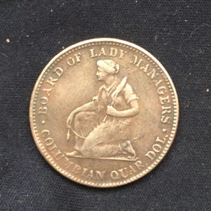 Puede incluir: Moneda de plata con la inscripción "Board of Lady Managers Columbian Quar. Dol." y la representación de una mujer arrodillada con un arco y una flecha.