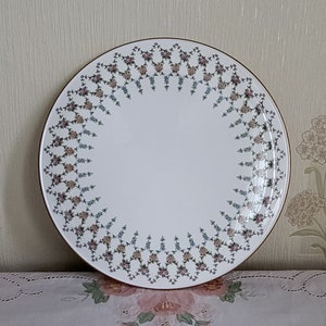 May include: A white ceramic plate with a gold rim and a floral pattern around the edge. The flowers are in shades of pink, blue, and green.