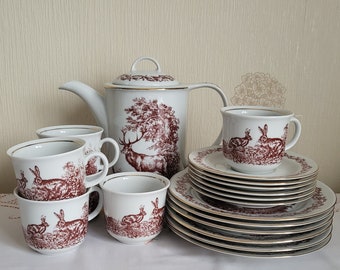 Könnte beinhalten: Ein weißes Porzellan-Tee-Set mit einem braunen und roten Design von Kaninchen und einem Hirsch in einem Wald. Das Set enthält eine Teekanne, vier Tassen und Untertassen.