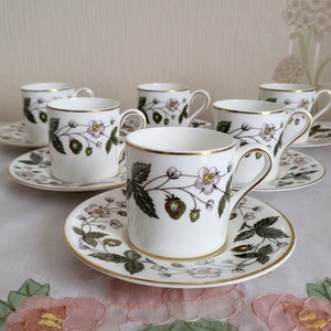 May include: Set of six white teacups and saucers with a floral pattern featuring strawberries and leaves. The cups and saucers have a gold trim.