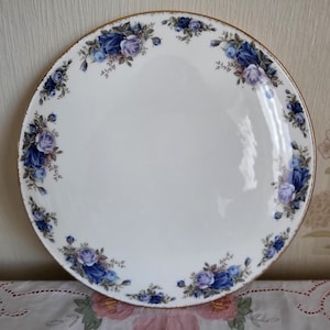May include: A white ceramic plate with a gold rim and a blue and purple floral design around the edge.