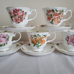 May include: Set of six white teacups and saucers with floral designs. Each cup features a different floral pattern, including pink roses, orange lilies, and purple flowers.