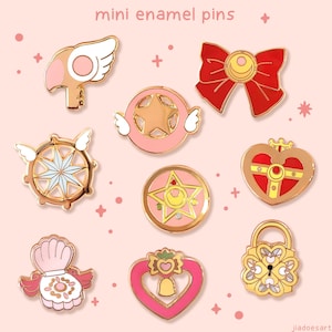 Puede incluir: Una colección de nueve mini alfileres de esmalte con diversas formas y diseños. Los alfileres presentan una paleta de colores rosa, dorado, rojo y blanco. Los alfileres incluyen una llave, un lazo, una estrella, una brújula, un corazón y un candado. El texto "mini enamel pins" está en la parte superior.