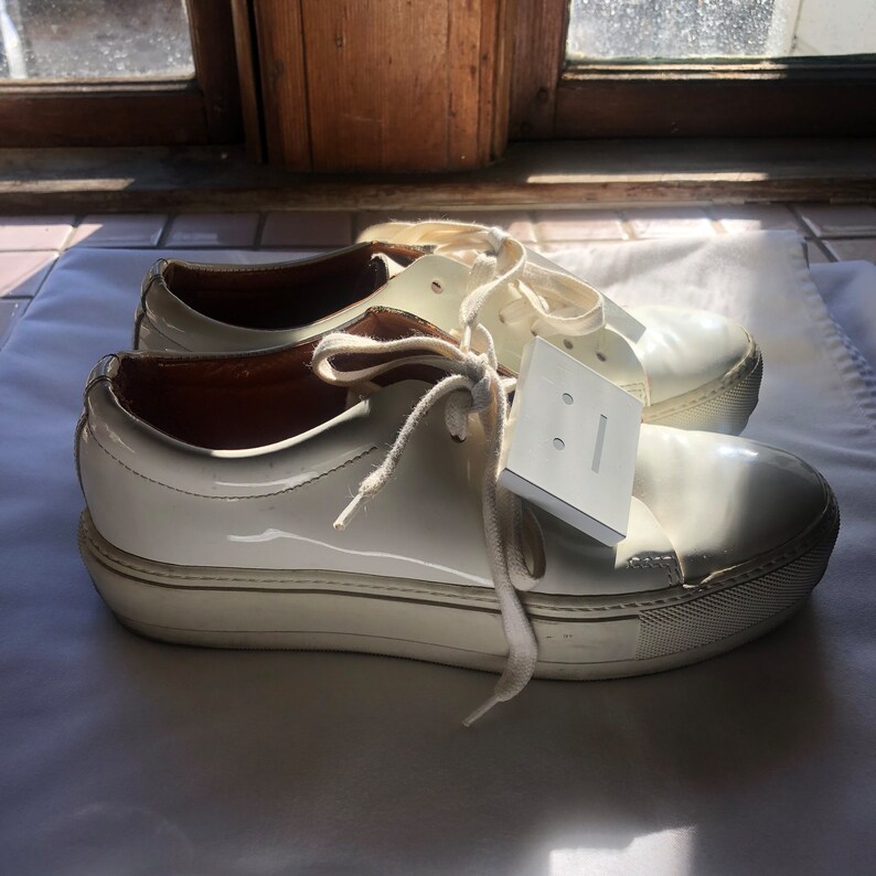May include: White patent leather platform trainers with white laces and a white tag that says "&mdash;&mdash;".