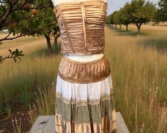 May include: A two-piece outfit on a mannequin. The top is a ruched, strapless corset in a bronze color. The skirt is a tiered design with white, green, and bronze panels. The outfit is displayed outdoors.