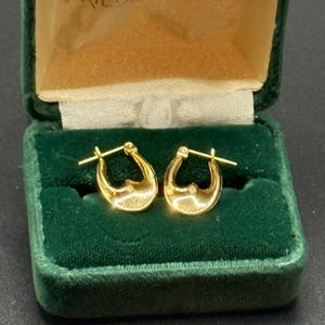 May include: A pair of gold hoop earrings displayed in a vintage green velvet jewelry box. The earrings have a polished finish and a classic design. The box has a gold satin interior and the name "FRIEDLANDERS" printed on the inside.