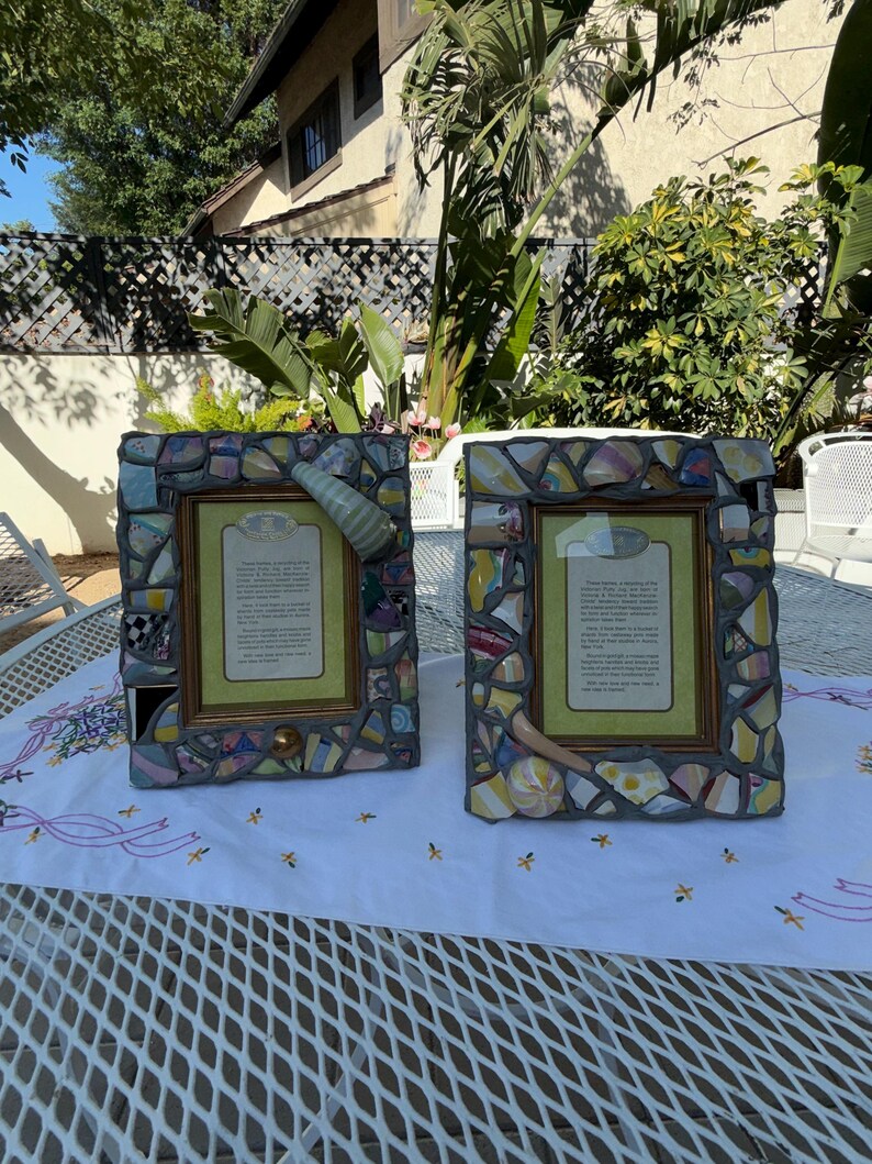 Puede incluir: Dos marcos de fotos rectangulares con un borde de mosaico hecho de fragmentos de cer&aacute;mica multicolor sobre lechada gris. Cada marco incluye una inserci&oacute;n de color verde claro con texto impreso y detalles decorativos de cer&aacute;mica.