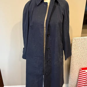 May include: A long navy blue coat with a button closure and a collar. The coat is on a white mannequin.
