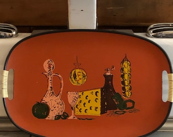May include: A vintage oval serving tray with a black rim and wooden handles. The tray features a colorful illustration of a still life with a bottle, a glass, a cheese block, a pepper mill, and a bunch of green olives.