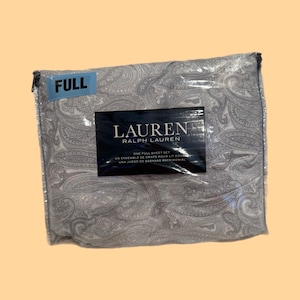 May include: A full sheet set by Lauren Ralph Lauren packaged in a clear plastic bag. The fabric features a grey and white paisley pattern. A blue sticker on the top left corner reads FULL, and a black label in the center displays the brand name.