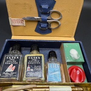 May include: A vintage Cutex manicure set in a leather case. The set contains nail polish remover, cuticle remover, and other nail care tools. The case is blue and tan. The scissors are held in place by a blue leather strap. The bottles contain 0.7 fl oz.