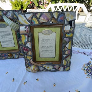 Puede incluir: Un marco de fotos rectangular con un borde de mosaico hecho de fragmentos de cer&aacute;mica coloridos fijados en lechada gris. El marco incluye un borde interior dorado y una inserci&oacute;n central con texto impreso sobre el reciclaje de jarras.