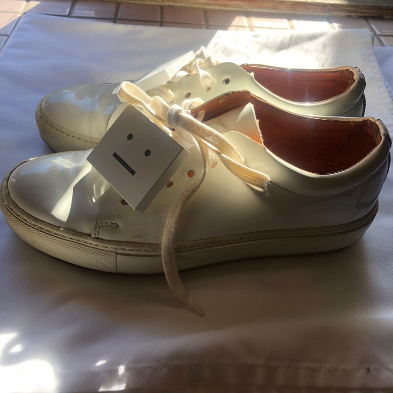 May include: White leather low-top trainers with white laces and a white tag that says "☹☹".
