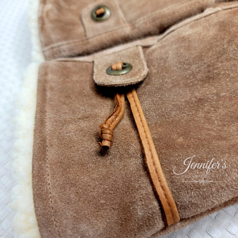 May include: Close-up of a brown suede bag with a leather strap and a metal buckle. The bag has a soft, fuzzy lining.