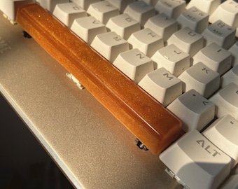 Könnte beinhalten: Eine goldfarbene Handballenauflage für die Tastatur mit glitzerndem Finish.