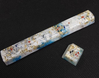 May include: A white and blue resin keycap with gold flakes and red and white fish designs. The keycap is part of a larger set of keycaps.