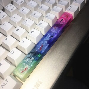May include: A colorful keyboard keycap with a blue, green, pink, and white abstract design. The keycap is made of resin and has a glossy finish.