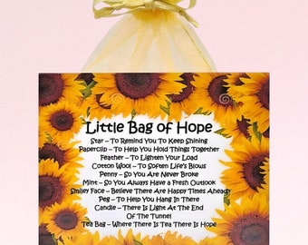 May include: A small, yellow, organza bag with a gold ribbon tied around the top. The bag contains a square tile with a sunflower design and the text "Little Bag of Hope" with a list of items and their symbolic meanings.