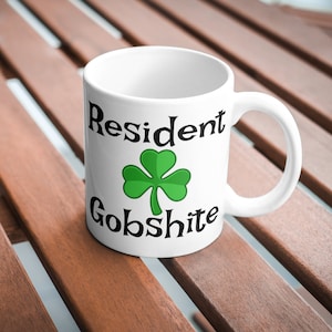 May include: White ceramic mug with a black shamrock and the text "Resident Gobsh*te" printed on it.