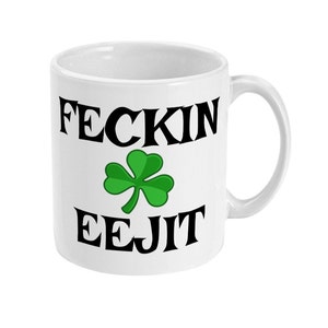 May include: White ceramic mug with black text that reads "FECKIN EEJIT" and a green shamrock.