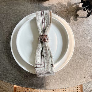 May include: A white dinner plate with a smaller white plate on top. A brown and white patterned napkin is tied around the plates with a brown napkin ring.