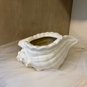 May include: White ceramic seashell planter. The planter is shaped like a large seashell with a wide opening and a textured surface.