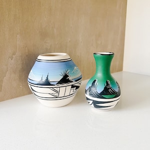 May include: Two hand-painted ceramic vases with geometric designs. The larger vase is blue and white with a mountain scene. The smaller vase is green and white with a mountain scene.