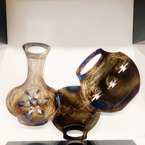 May include: Three metal wall sculptures in the shape of stylized pots. The pots are brown and gold with a blue iridescent finish. The pots have geometric designs and are arranged in a cluster.