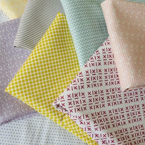Può includere: Una collezione di campioni di tessuto piegati con vari motivi, tra cui pois gialli, croci bordeaux, strisce grigie, gocce di pioggia azzurre, triangoli rosa pallido e forme geometriche viola, disposti in una composizione a strati.