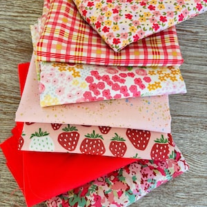 Peut inclure: Un empilement de carrés de tissu colorés. Motifs : vichy rouge et blanc, imprimés floraux roses et jaunes, tissu rose à pois blancs, imprimé fraises et tissu rouge uni. Idéal pour le patchwork ou la couture.