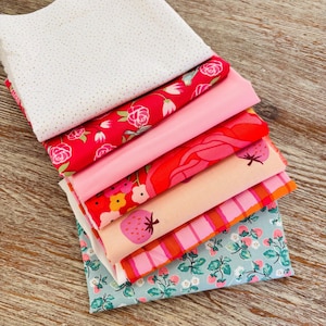 Peut inclure: Un empilement d'échantillons de tissus colorés. Les tissus présentent divers motifs, notamment des pois dorés, des roses, des fraises et des rayures. Les couleurs incluent le blanc, le rouge, le rose et le bleu. Les tissus sont disposés sur une surface en bois.