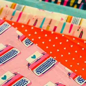 Peut inclure: Une collection de tissus aux motifs colorés. Les tissus présentent des motifs de machines à écrire, de cœurs et de formes abstraites dans des tons de rose, de rouge, de bleu et de turquoise. Les tissus sont empilés, mettant en valeur la variété des motifs.