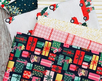 May include: A stack of folded cotton fabric pieces featuring various Christmas-themed prints, including nutcrackers, red trucks carrying trees, gold foil accents, pink houndstooth patterns, and a dark navy background with colorful gift boxes.