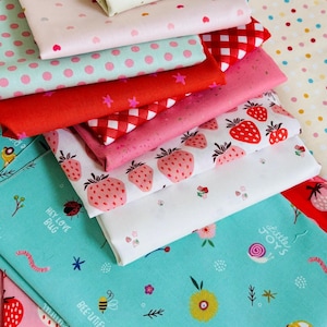 Peut inclure: Une pile de tissus colorés avec divers motifs. Les motifs comprennent des fraises, des pois, du vichy et des motifs floraux. Les couleurs vont du rouge et du rose au turquoise et au blanc. Certains tissus comportent du texte comme "Hey Love Bug" et "Enjoy the Ride".