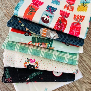 Peut inclure: Une pile de tissus colorés sur le thème de Noël. Les motifs incluent des crackers, des chats dans des voitures et des couronnes de Noël. Les couleurs sont le rouge, le vert, le bleu et le blanc, parfaites pour les travaux manuels et la couture.