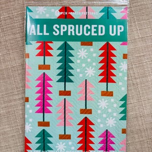 May include: A quilt pattern booklet titled All Spruced Up by Pen Paper Patterns. The cover features a light blue background with a repeating graphic print of stylized Christmas trees in red, pink, and dark green, accented by white snowflakes.