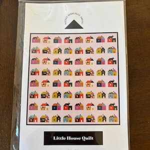 May include: A quilt pattern packet titled Little House Quilt by Alexia Marcelle Abegg, measuring 70" x 72". The cover features a grid of small, colorful house illustrations in various patterns and hues set against a light pink background.