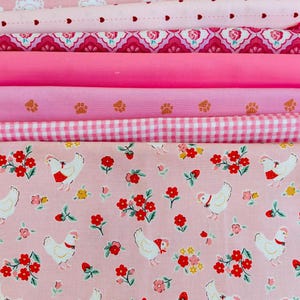 Peut inclure: Plusieurs rouleaux de tissu rose avec divers motifs. Les motifs comprennent des fleurs, des cœurs, des empreintes de pattes, du vichy et un imprimé poulet avec des fleurs rouges. Les tissus varient dans les tons de rose, créant une esthétique cohérente et charmante.