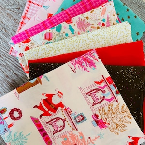 May include: A stack of folded fabric squares featuring various holiday-themed patterns. Designs include Santa Claus by a fireplace, gold stars on teal, red and pink houndstooth, white with gold branches, and solid red and dark brown with gold flecks.