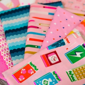 Puede incluir: Una colección de muestras de tela coloridas con varios patrones. Los diseños incluyen rayas onduladas, lápices, corazones e ilustraciones de cajas de cerillas en tonos rosa, azul, verde y naranja. Las telas están dobladas y apiladas, mostrando la variedad de estampados.