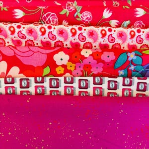 Peut inclure: Une pile de tissus à motifs roses et rouges. Les motifs comprennent des motifs floraux, des cachemires et une impression de bocaux rouges. La couche inférieure est un tissu magenta uni avec des paillettes dorées.