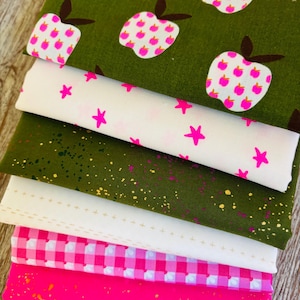 Könnte beinhalten: Ein Stapel aus sechs gefalteten Stoffstücken mit verschiedenen Mustern. Die oberste Schicht ist olivgrün mit weißen und pinken Apfelmustern. Darunter befinden sich weißer Stoff mit pinken Sternen, olivgrün mit goldenen Sprenkeln, weiß mit goldenen Pluszeichen, pink-weißes Vichy-Karo und eine einfarbige, kräftig pinke Basis mit goldenen Sprenkeln.