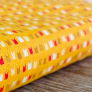 May include: Yellow fabric with a repeating pattern of small red, white, and brown crowns.