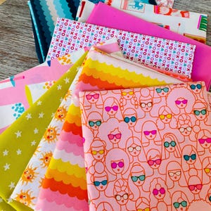 Puede incluir: Una colección de cuadrados de tela doblados con varios patrones, incluyendo un estampado rosa de rostros con gafas de sol, ondas amarillas y naranjas, estrellas blancas sobre fondo verde lima, soles y un diseño ondulado azul oscuro.
