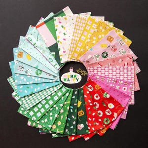 May include: A circular arrangement of colorful fabric squares with holiday-themed patterns. The fabrics feature gift boxes, ornaments, and other festive designs in shades of green, pink, yellow, and blue. A central ornament-shaped tag reads "Merry Happy."